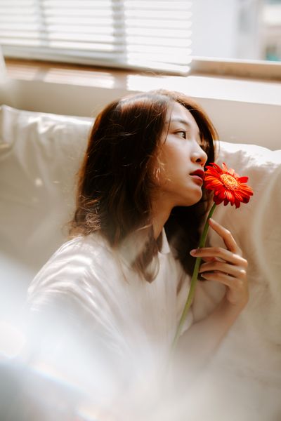 woman sitting on couch holding red flower up to her mouth